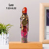 A tall glass bottle filled with red and purple crystals and topped with a gold lion charm