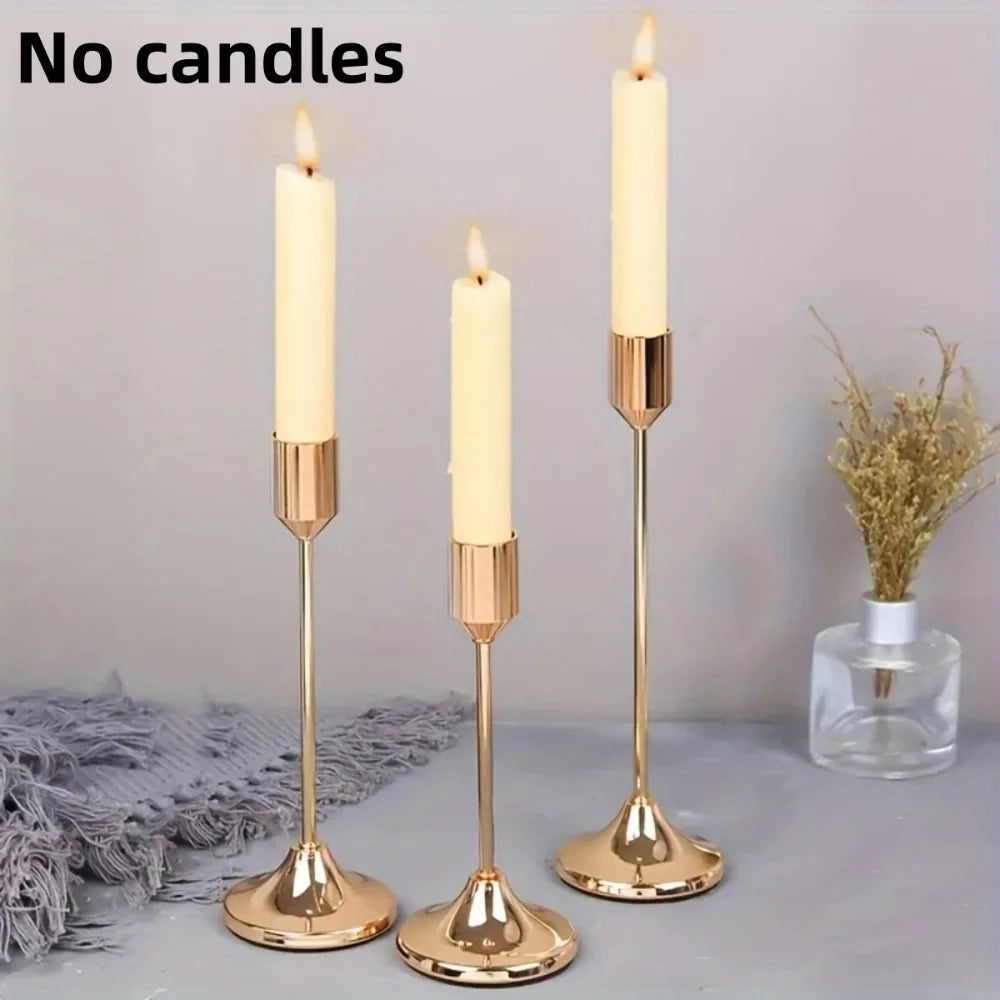 A set of three gold-toned minimalist candle holders with white taper candles displayed on a gray surface.