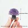 A hand holds a natural crystal mushroom tree sculpture showing purple crystals on a dark base.