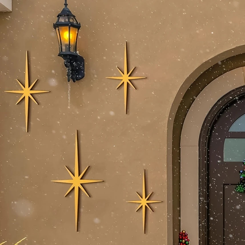 A set of four gold metal star wall art pieces mounted on a beige stucco wall next to an antique lantern.
