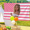 A woman in a white top holds a large American flag banner with stars and stripes, surrounded by yellow and orange balloons.