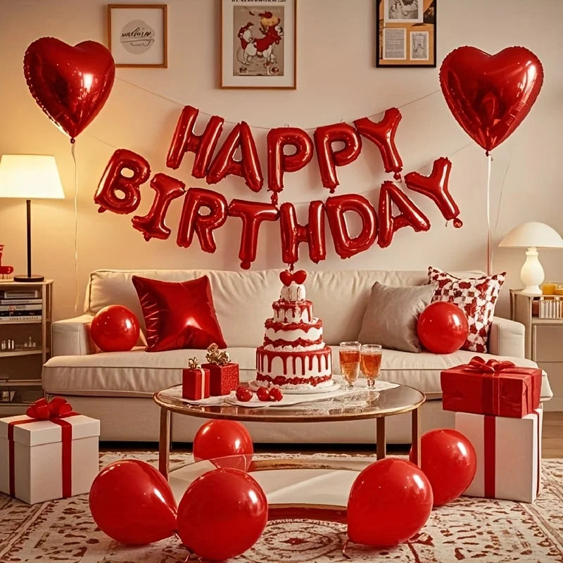 A red heart and star foil balloon decoration set strung across a wall above a sofa with gifts and red balloons on the floor.