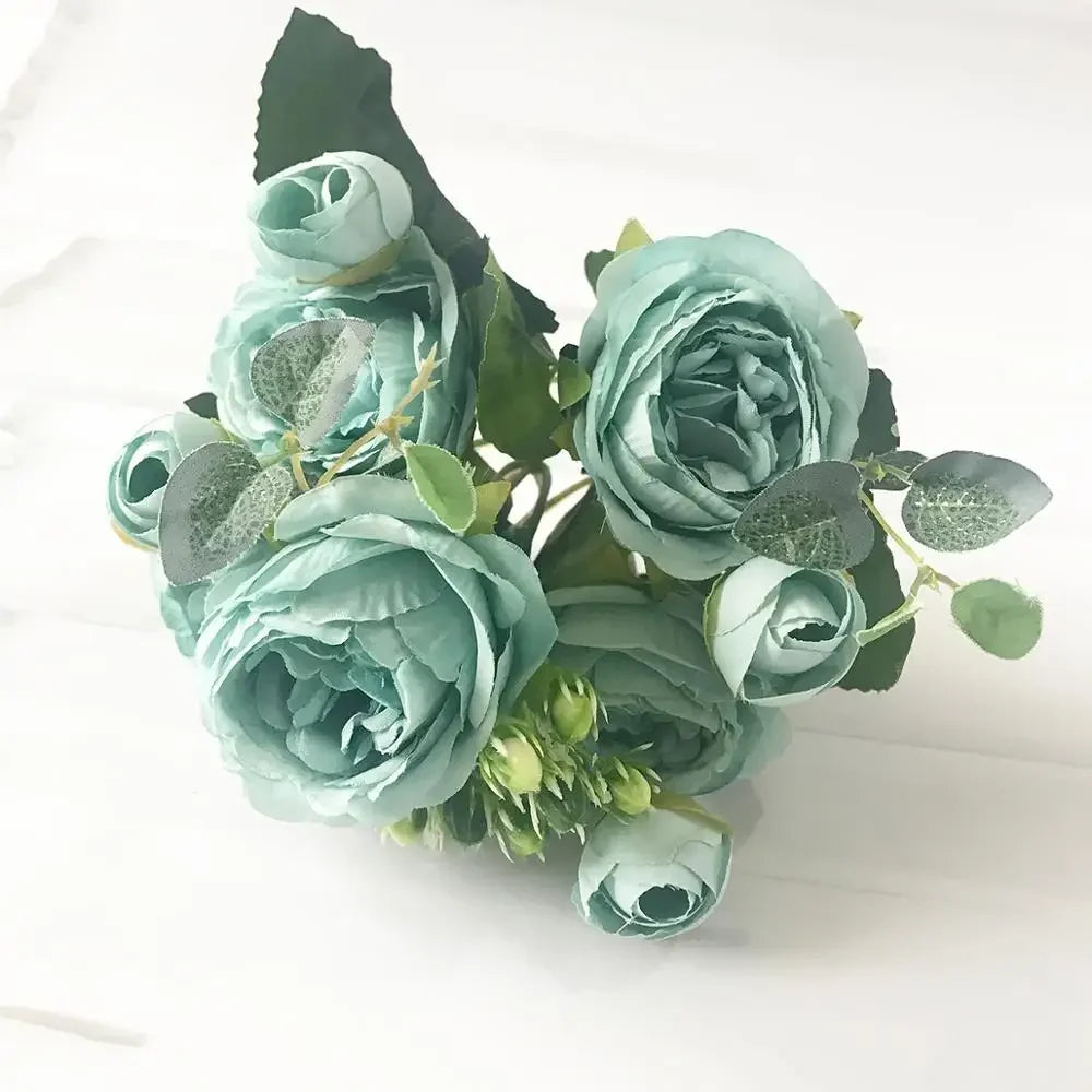 A bouquet of dusty blue silk rose and peony artificial flowers with green leaves.