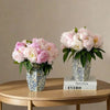 A floral arrangement of pink and white peonies in a blue and white porcelain vase on a wooden table.