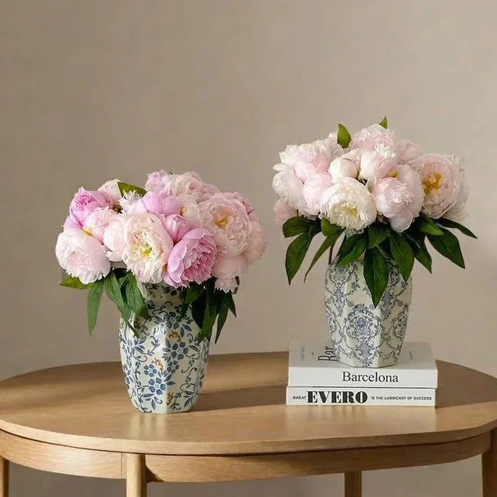 A floral arrangement of pink and white peonies in a blue and white porcelain vase on a wooden table.