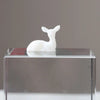 A white resin ornament shaped like an elk or deer stands on a clear glass base.