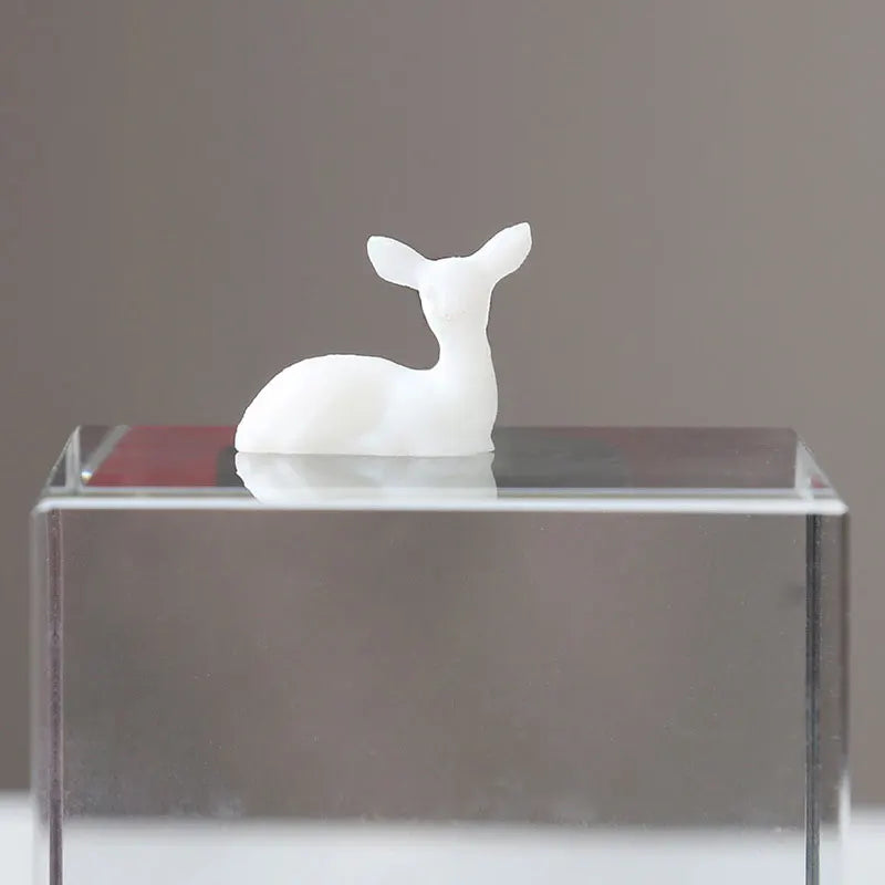 A white resin ornament shaped like an elk or deer stands on a clear glass base.