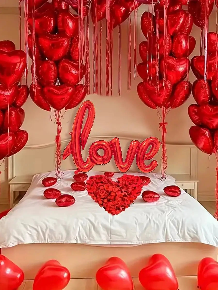 A display of red heart-shaped balloons and rose petals decorating a bed for a romantic celebration.