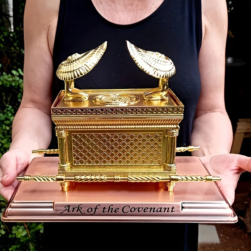 A golden metal statue of the Ark of the Covenant resting on a pink base.