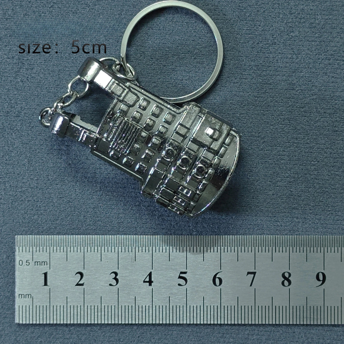 Silver alloy gun model miniature keyring with a circular loop and a ruler for scale.