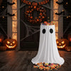 A white ghost-shaped fabric display with black eyes sits on a wooden floor in a Halloween decorated setting.