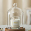 A clear glass aromatherapy candle holder with a white scented candle sits on a round wooden base.