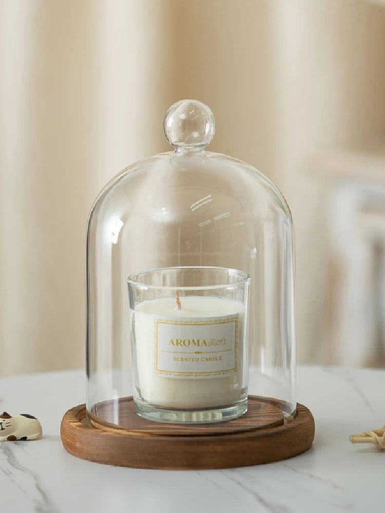 A clear glass aromatherapy candle holder with a white scented candle sits on a round wooden base.