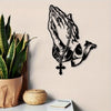 Black metal wall art depicting praying hands with a cross, displayed next to a potted plant and a woven basket.