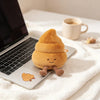 A small, round, golden-brown plush toy shaped like a toilet paper poop plunger resting on a laptop and white fabric.