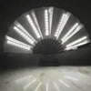 An illuminated folding hand fan with LED lights casting light patterns on a marble surface.