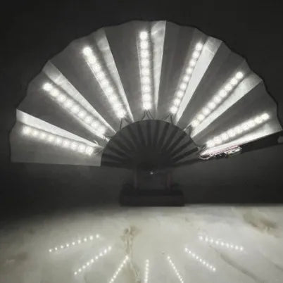 An illuminated folding hand fan with LED lights casting light patterns on a marble surface.