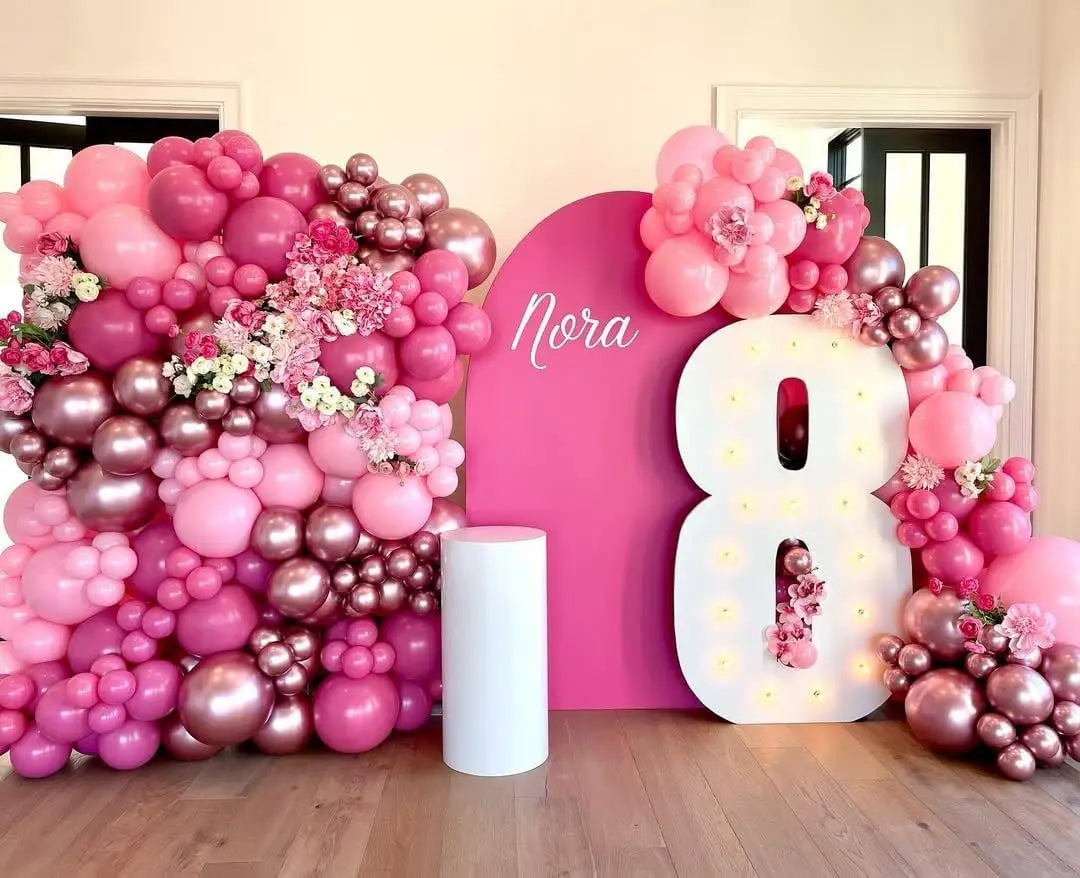 A vibrant pink and rose gold balloon garland featuring various sized balloons and large number balloons for a celebration.
