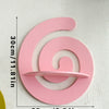 A pink, cherry-shaped wooden wall shelf with a spiral design mounted on a white wall.