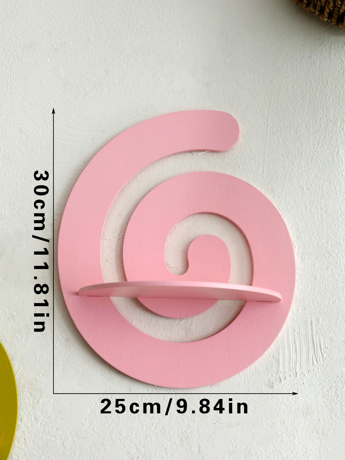 A pink, cherry-shaped wooden wall shelf with a spiral design mounted on a white wall.