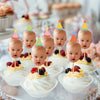 A display of cupcakes with colorful party toppers on a tiered stand for a baby's first birthday celebration.