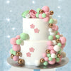 A two-tiered cake decorated with pink and green foam balls and floral accents.