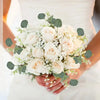 A bridal bouquet of white roses and eucalyptus leaves held by a person.