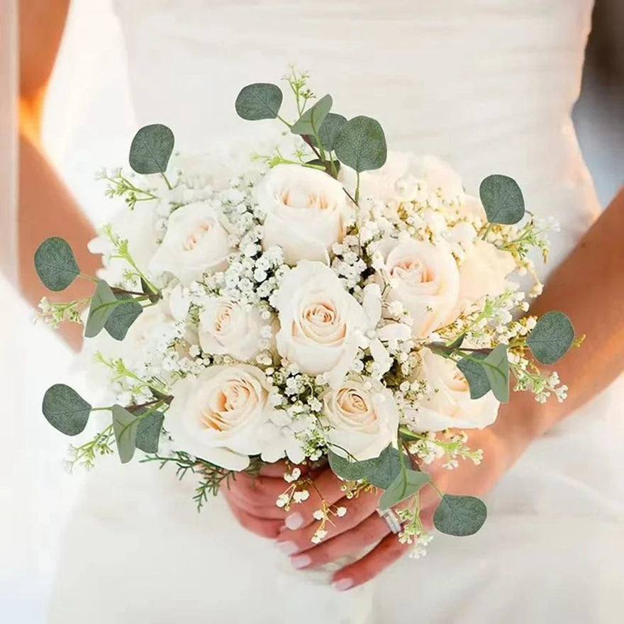 A bridal bouquet of white roses and eucalyptus leaves held by a person.