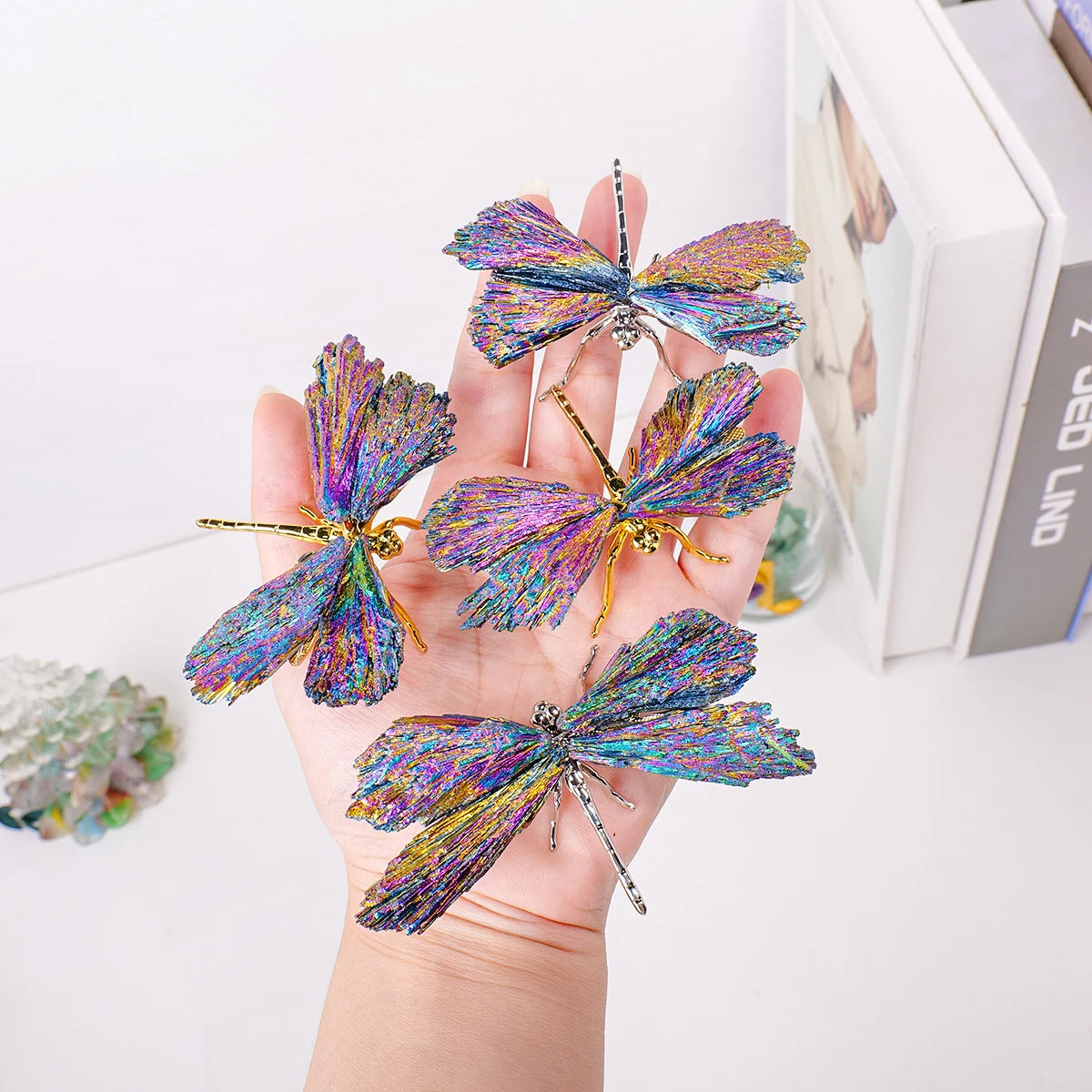 A hand holds a sparkling natural crystal tourmaline dragonfly figurine with iridescent blue and purple wings.