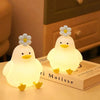 A glowing white duck LED night light with a flower on top resting on a book.