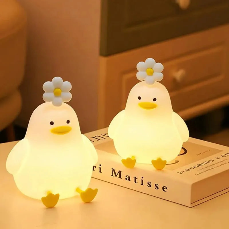A glowing white duck LED night light with a flower on top resting on a book.