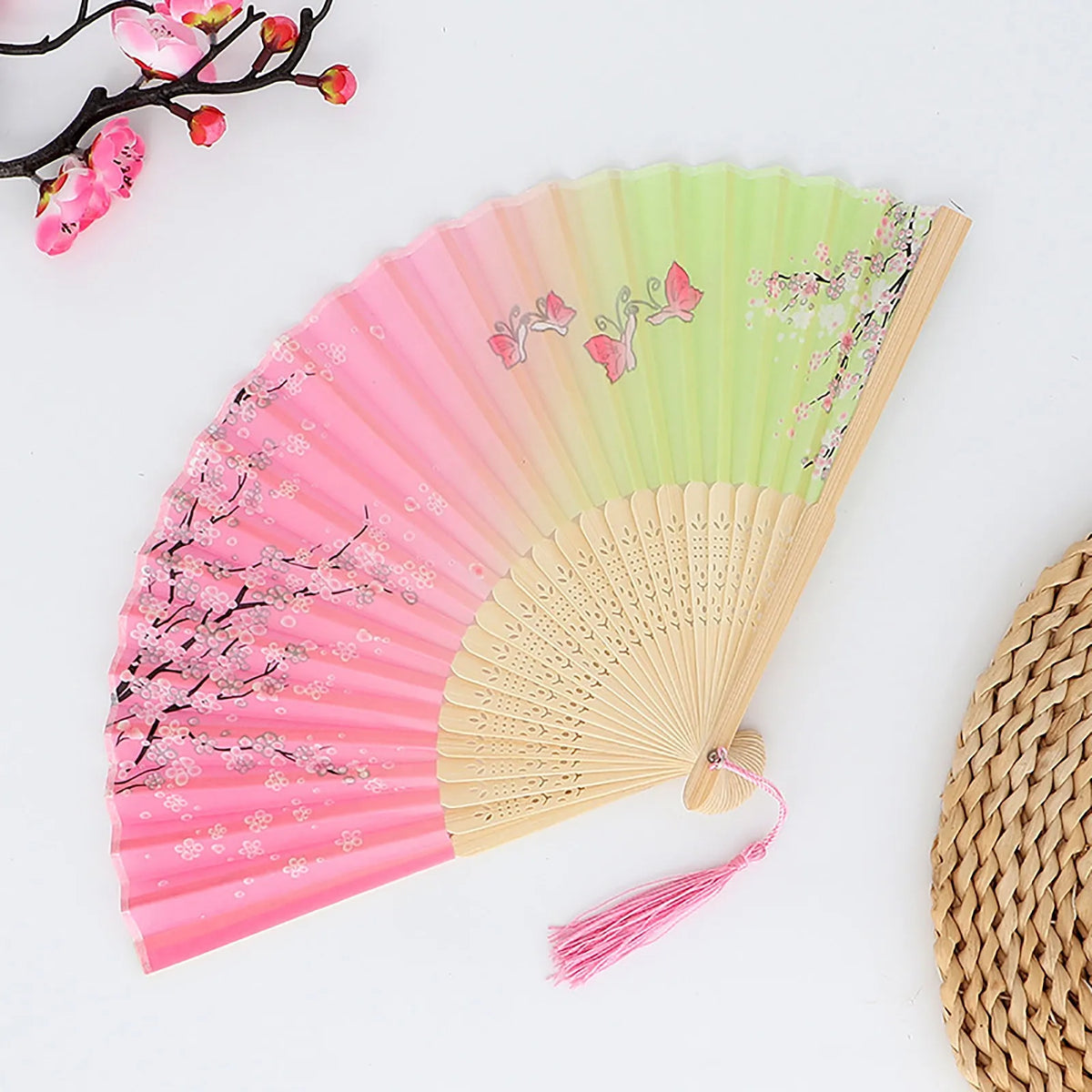 A vintage bamboo folding fan with a rainbow gradient fabric featuring pink and green tones and floral patterns.