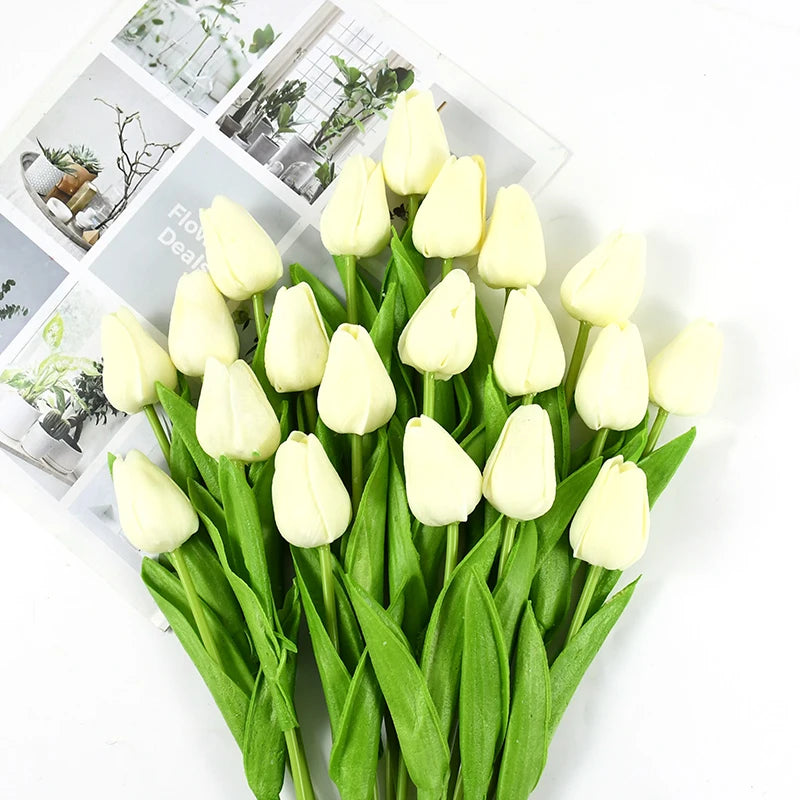 A bouquet of white artificial tulips with green stems and leaves displayed on a white background.