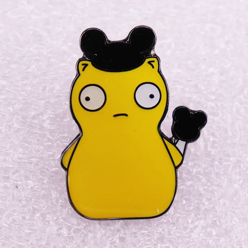 A yellow enamel pin badge shaped like a cartoon character with black ears and a surprised expression.