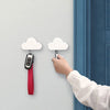 A hand is hanging a magnetic cloud key hanger onto a white wall next to a blue door frame.