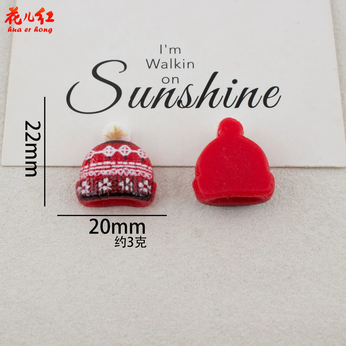 A red resin Christmas bell and a white knitted crown are displayed on a white card.