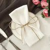 A set of ten white fringed cotton napkins tied with twine rests on a plate next to a dark gray cloth.