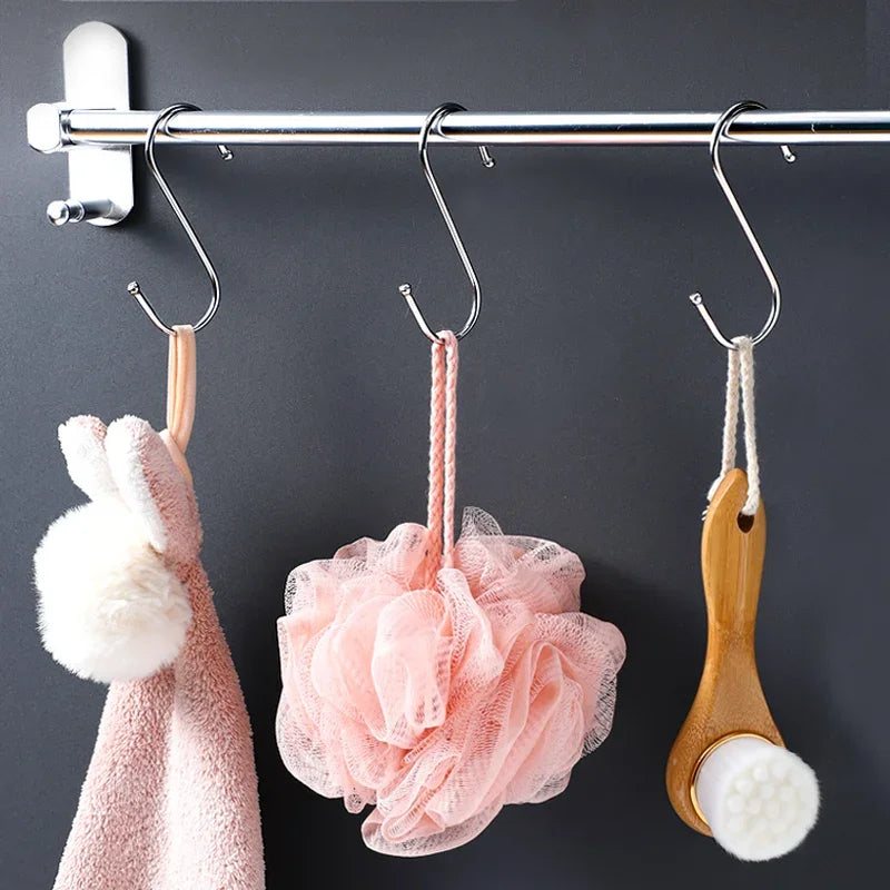 A set of S-shape stainless steel hanging hooks is displayed against a dark background, featuring pink and white fabric items.