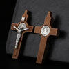 A wooden crucifix pendant featuring a figure of Christ and St. Benedict on a cross, set against a dark background.