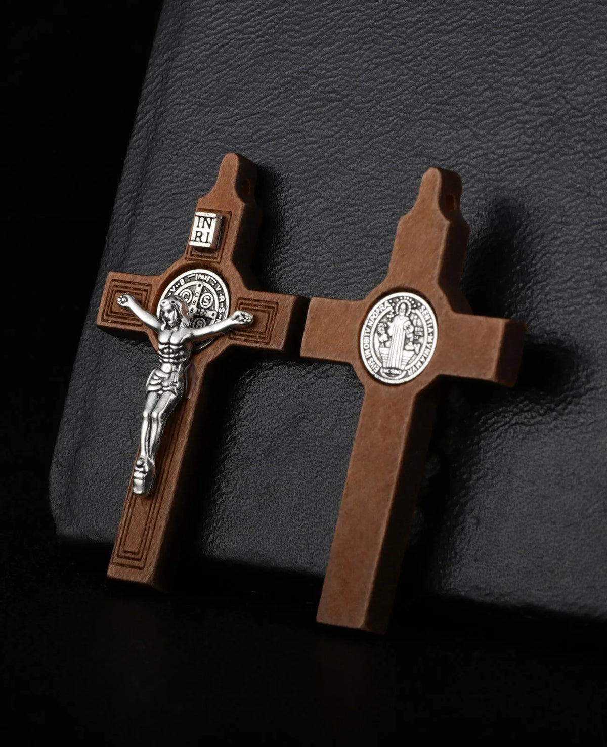 A wooden crucifix pendant featuring a figure of Christ and St. Benedict on a cross, set against a dark background.