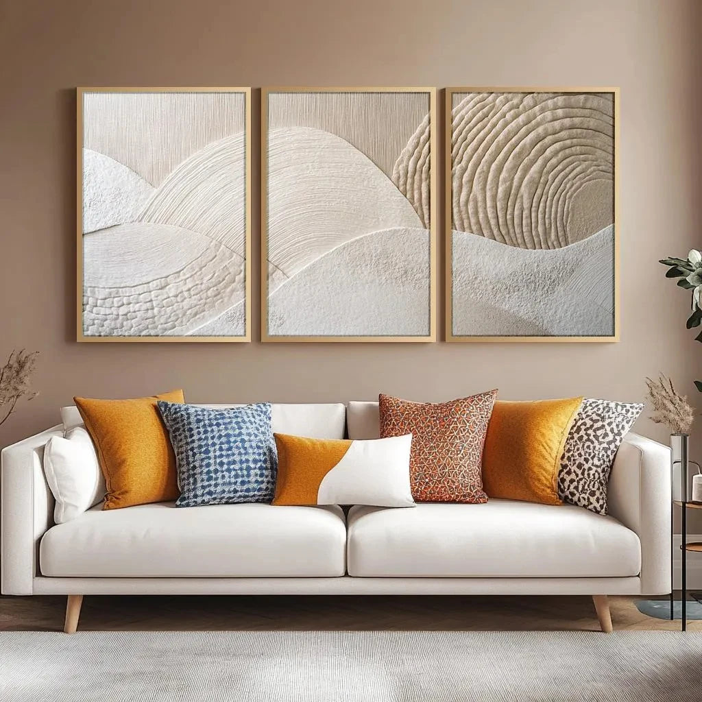 A set of three framed abstract canvas prints featuring beige and white textured mountain wave patterns displayed above a ligh