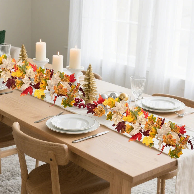 An artificial maple leaf garland in autumn colors is displayed on a wooden table setting.