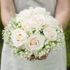 A bouquet of cream and blush roses accented with baby's breath flowers held by a person.