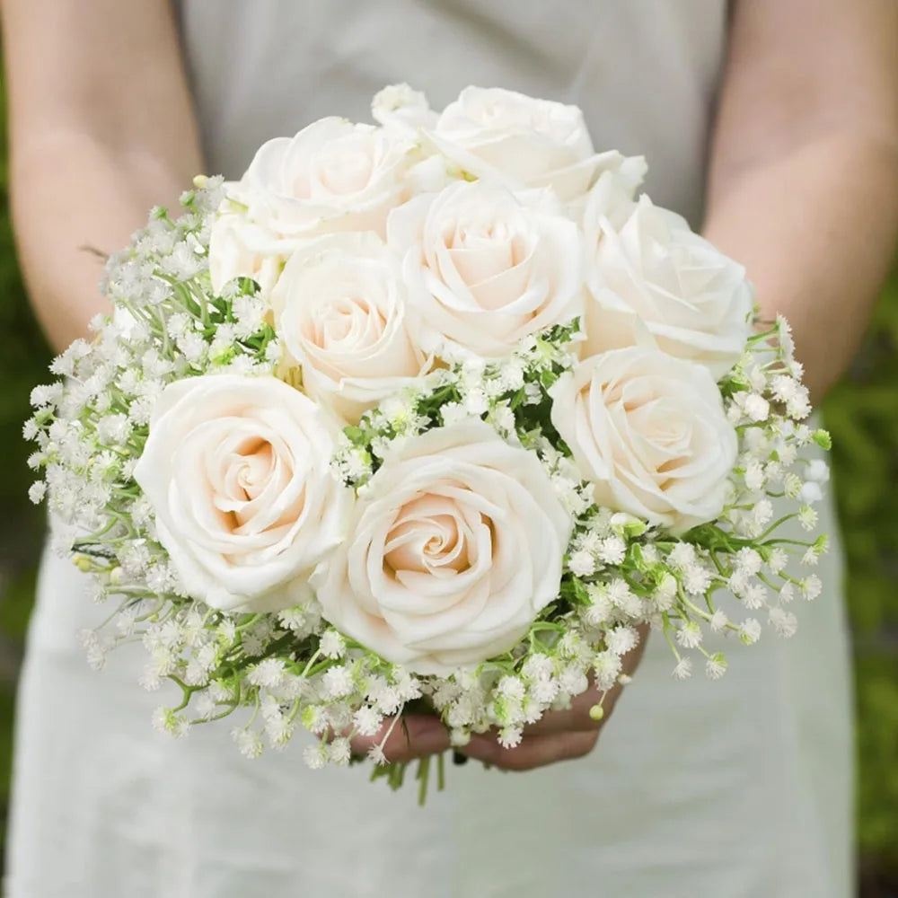 A bouquet of cream and blush roses accented with baby's breath flowers held by a person.