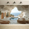 A natural cave opening frames a view of the blue sea and a small infinity pool with lounge chairs.