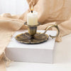 Porte-bougie lotus en fer forgé vintage avec bougie blanche, sur un bloc blanc et drapée de lin beige.