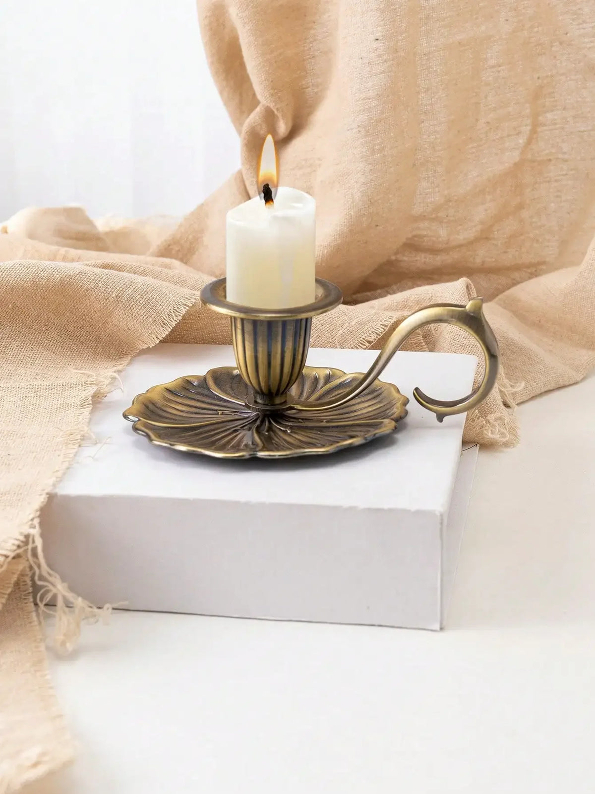 Porte-bougie lotus en fer forgé vintage avec bougie blanche, sur un bloc blanc et drapée de lin beige.