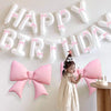 A young girl stands in front of a white balloon banner spelling out Happy Birthday, surrounded by pink and white balloons.