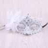 Silver rhinestone masquerade mask with white feather decoration on a light wooden surface