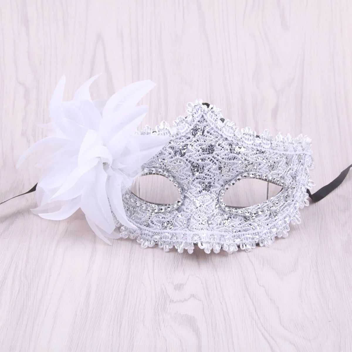 Silver rhinestone masquerade mask with white feather decoration on a light wooden surface